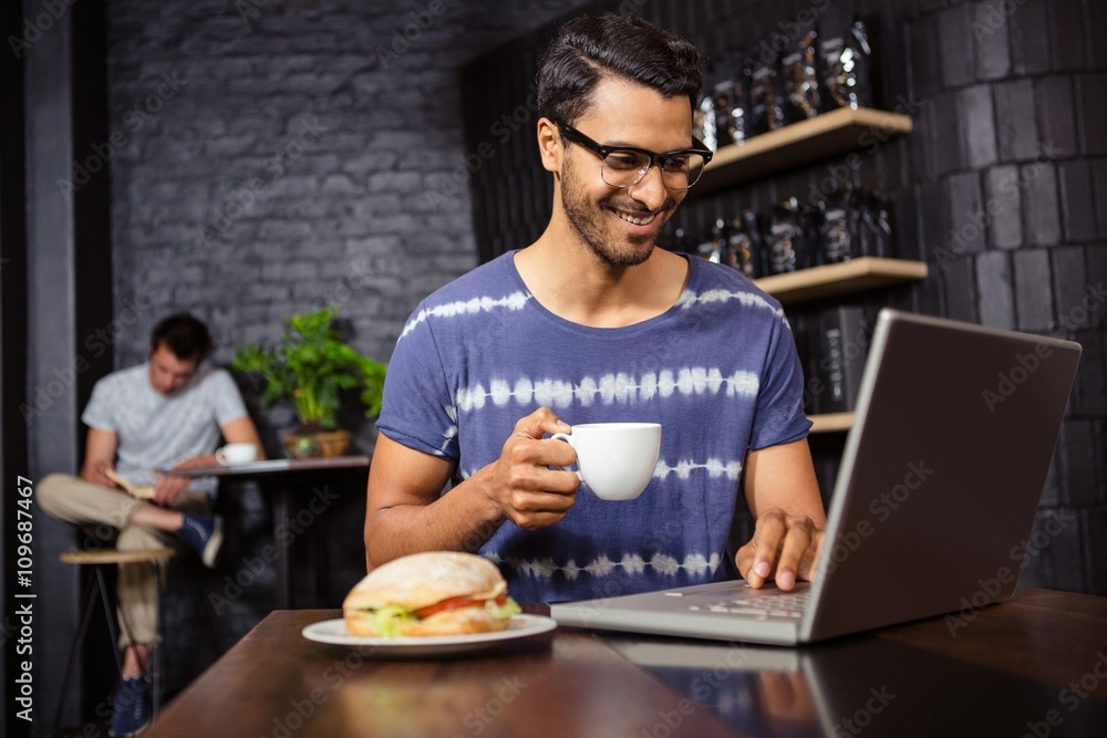 Fototapeta premium Man using a laptop and drinking coffee