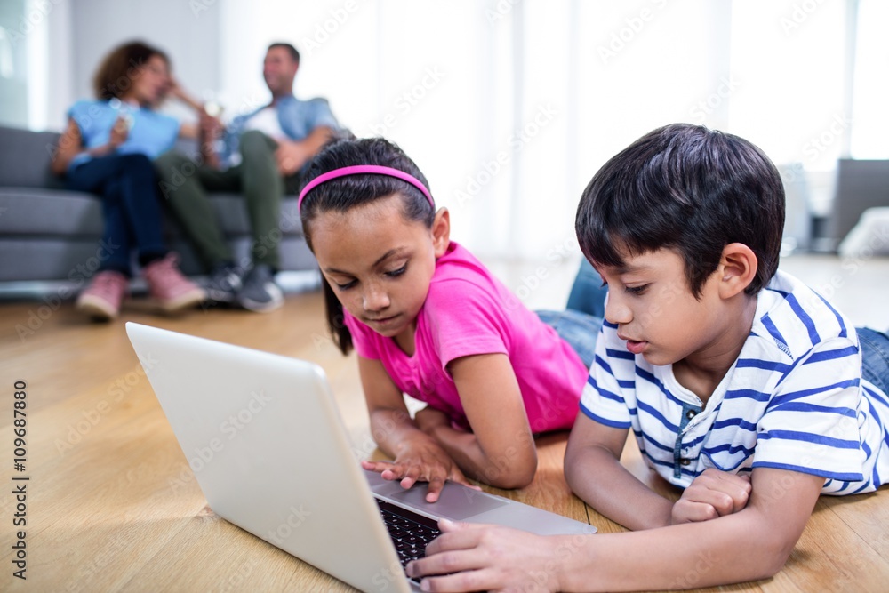 Brother and sister lying on floor and using laptop