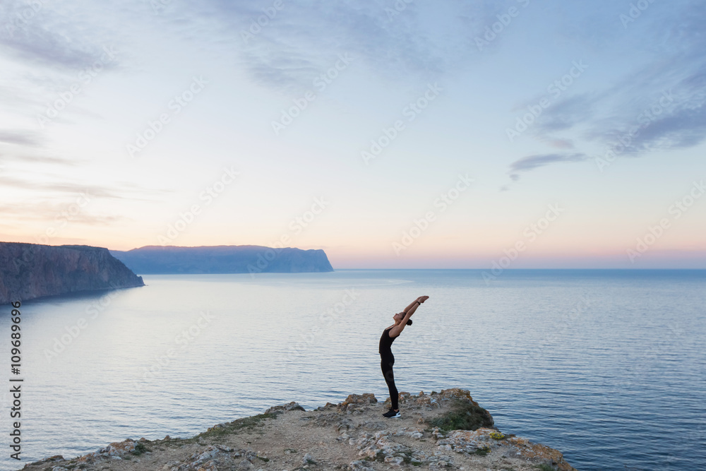 Woman practicing pose from yoga on the edge of the cliff meeting
