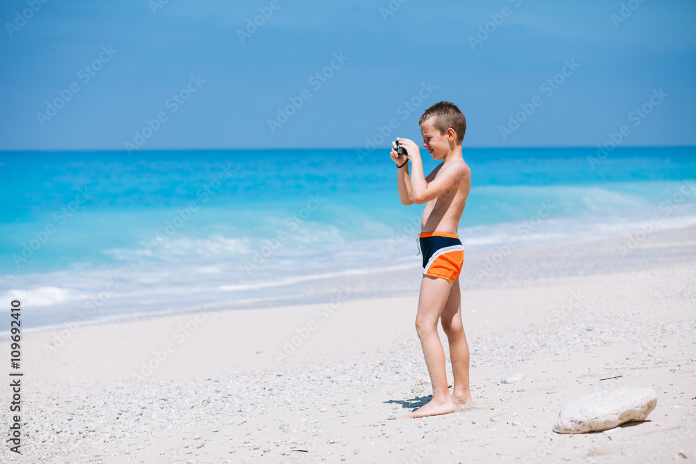 Beach vacation dream. Handsome young boy enjoying in beautiful tropical beach and taking some photos with his camera.