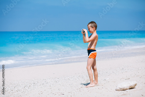 Beach vacation dream. Handsome young boy enjoying in beautiful tropical beach and taking some photos with his camera.