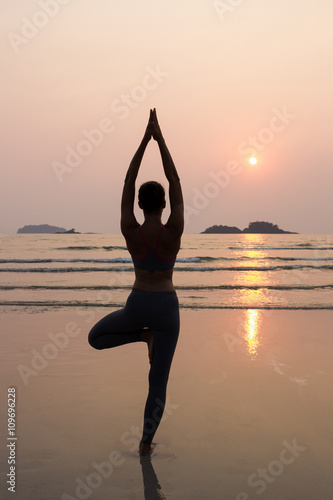 Young slim woman practicing pose from yoga on the beach at sunse