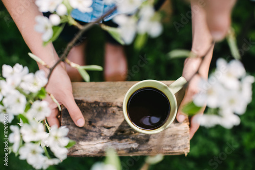 Girl holds green cup of coffee on a wooden stand in the garden