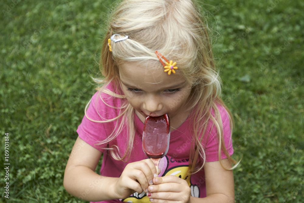 Beautiful little child blond girl eats - licking icecream in the summer Beautiful little child blond girl eats - licking icecream in the summer