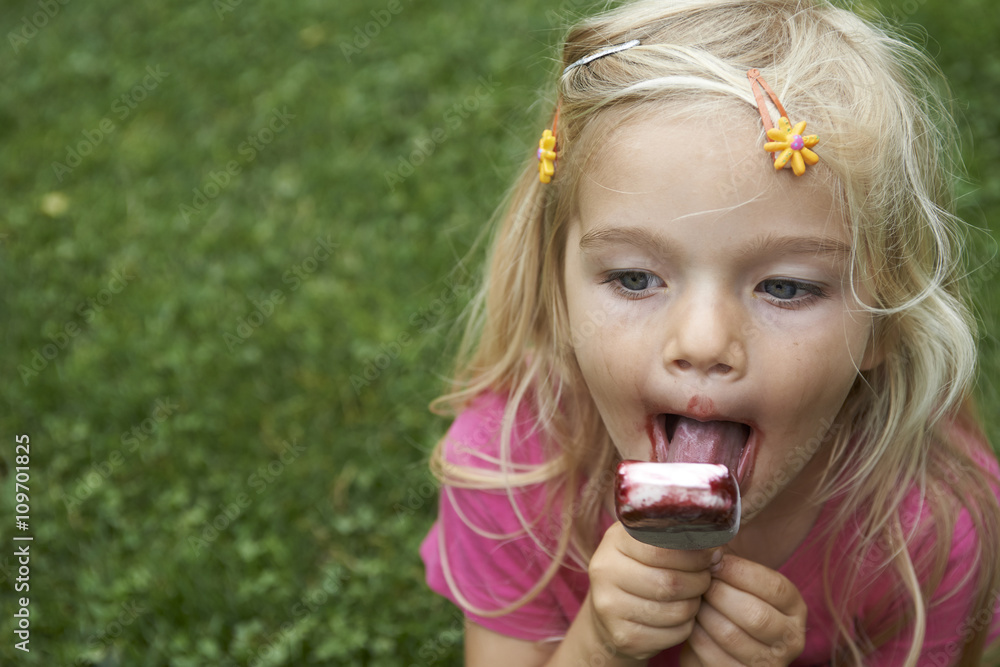 Beautiful little child blond girl eats - licking icecream in the summer Beautiful little child blond girl eats - licking icecream in the summer