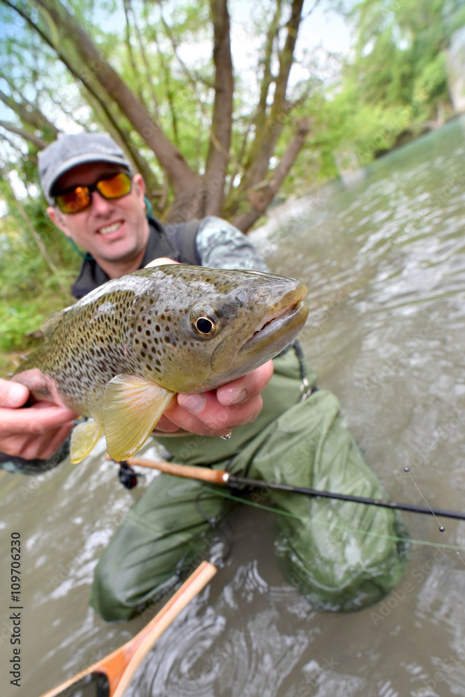 Fly-fisherman holding fario trout caught in river