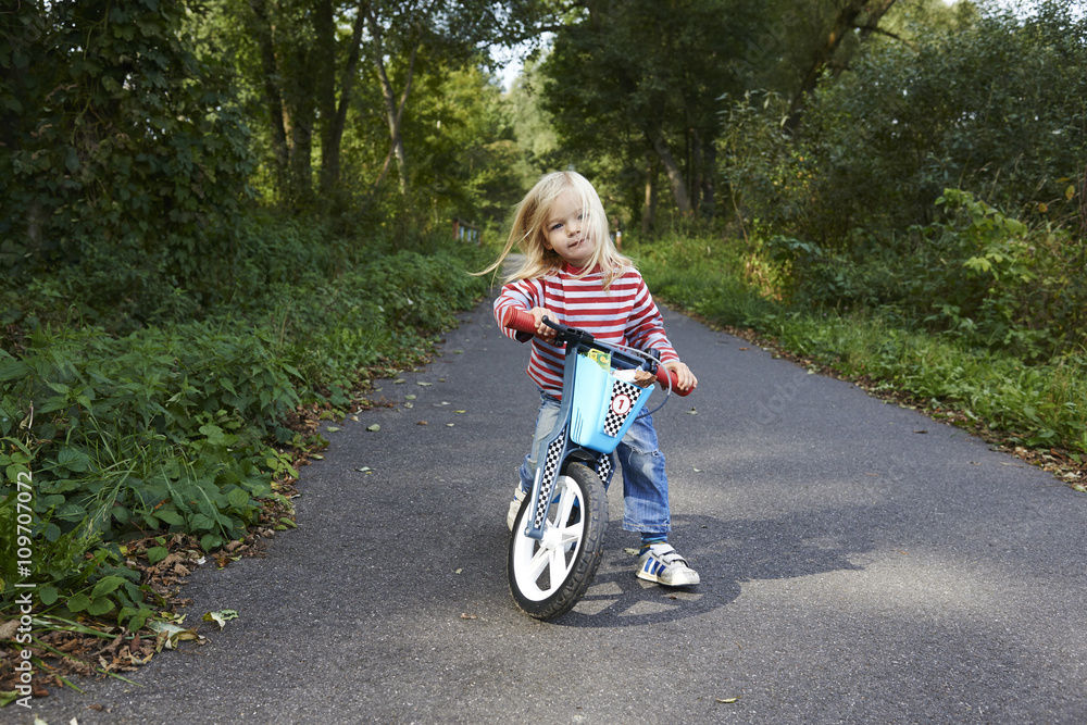 Cute little blond girl riding runbike a bicycle path, active kids sport Cute little blond girl riding runbike a bicycle path, active kids sport