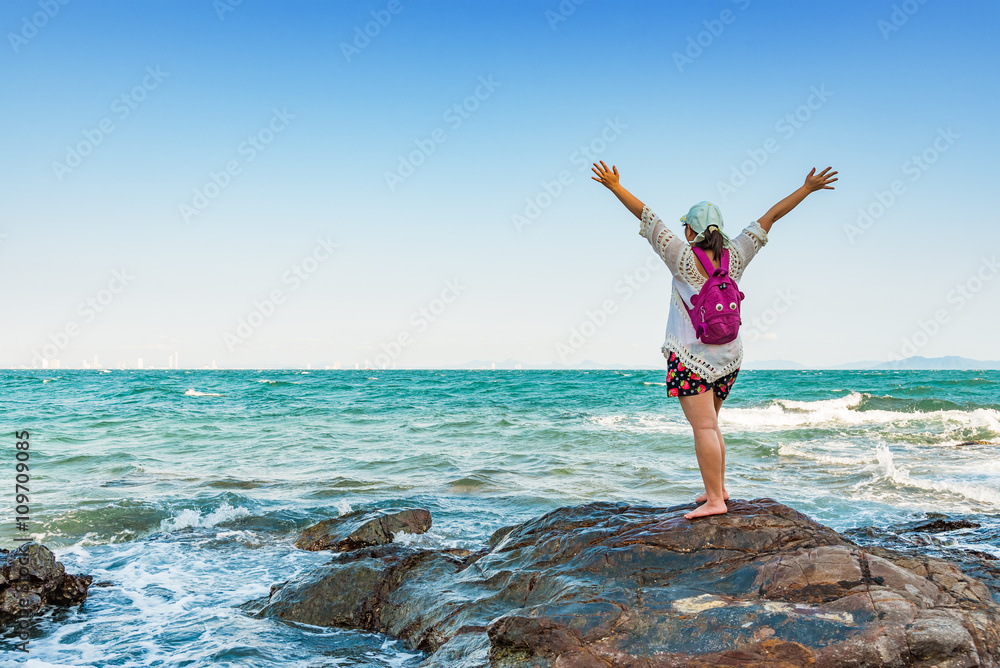 Happy young woman spreading hand on the rock beach for relaxed.