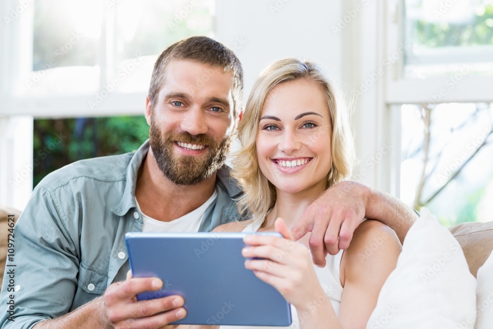 Portrait of couple sitting on sofa and using digital tablet