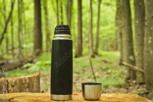 Thermos and a cup of coffee in the green forest in summer campaign