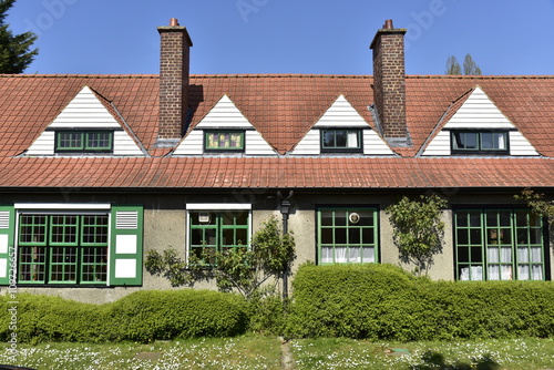 L'une des habitations jumelées typiquement anglais avec lucarnes triangulaires et chassis noirs-verts entouré de verdure à la Cité-Jardin du Logis à Watermael-Boitsfort 