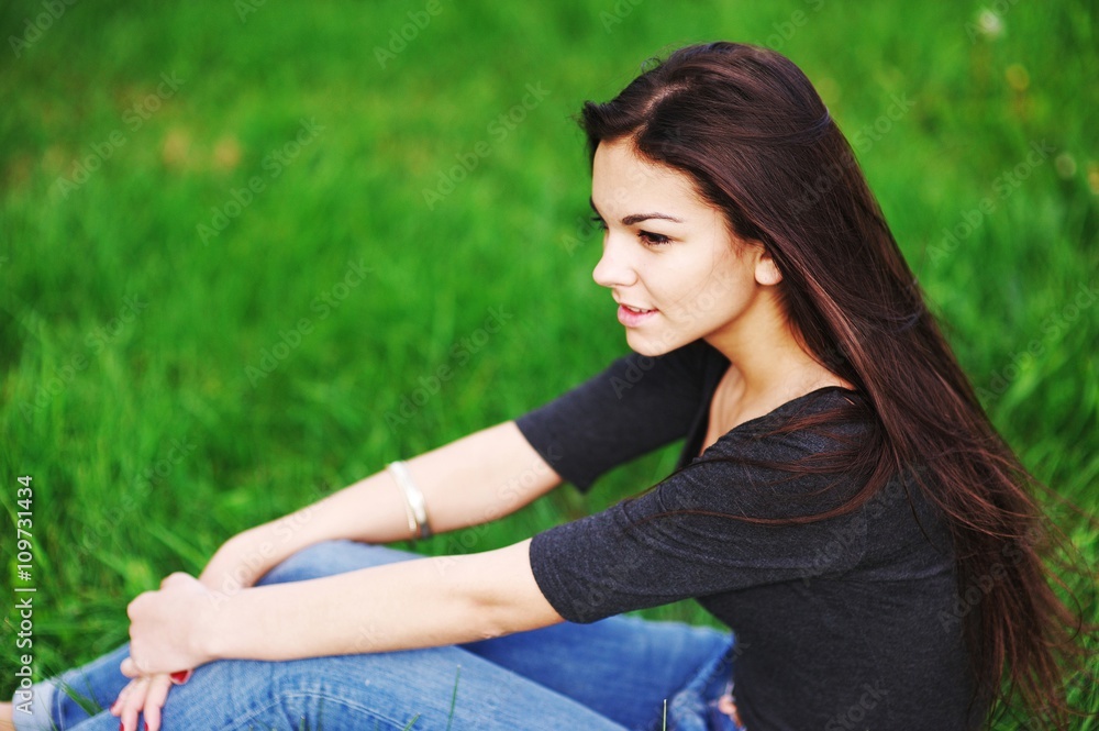 beautiful girl in a black shirt sitting on the grass and stares dreamily beautiful girl in a black shirt sitting on the grass and stares dreamily