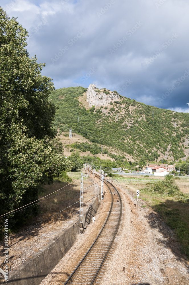 Fototapeta premium Iberian gauge railway track between Leon and Gijon on its way through La Pola de Gordon, Leon Province, Spain. In the background can be seen the town of Puente de Alba