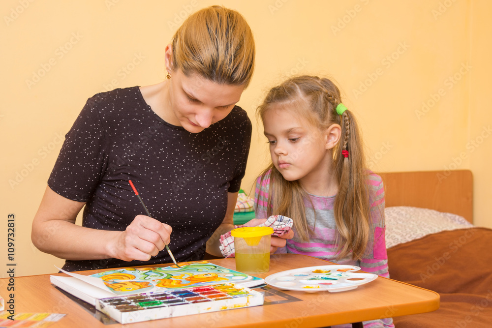 Girl artist teaches a little girl at the table as a draw watercolor on paper Girl artist teaches a little girl at the table as a draw watercolor on paper