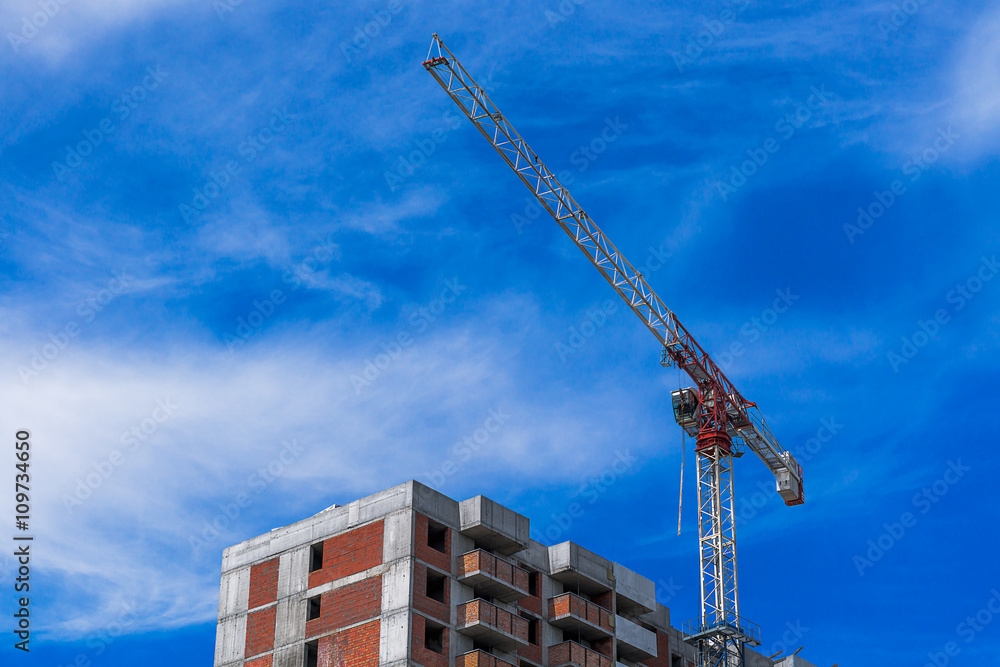Hoisting crane working on building construction on blue cloudy sky background
