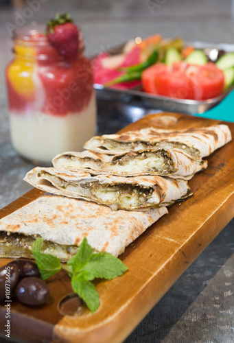 Lebanese manakeesh manouche with zaatar, served on a rustic wooden board with mint leaves, olives and a strawberry smoothie.