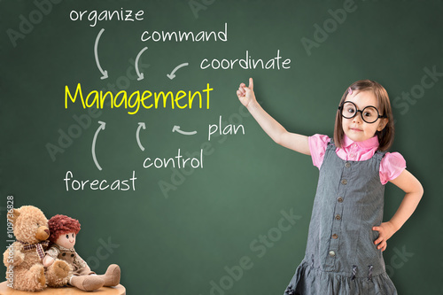 Cute little girl wearing business dress and showing management skill and responsibility on green chalk board.