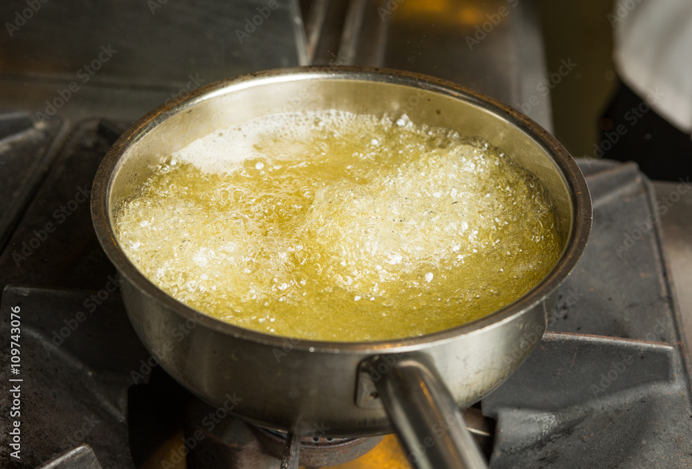 A pan of hot bubbling boiling oil in a silver pan on a hob. A pan of hot bubbling boiling oil in a silver pan on a hob.