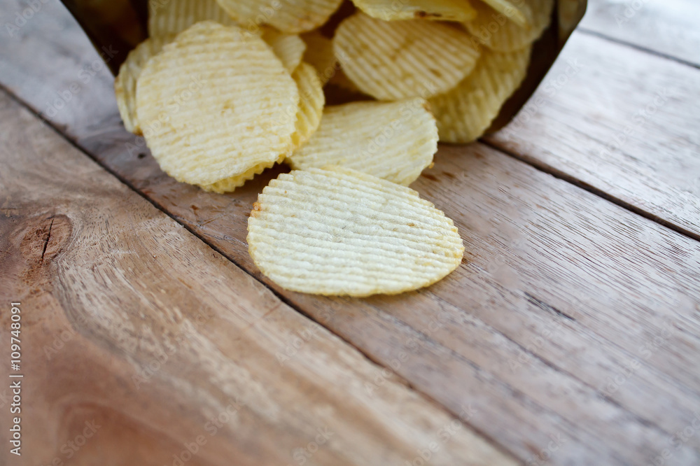 Opened pack with potato chips over wooden table Opened pack with potato chips over wooden table