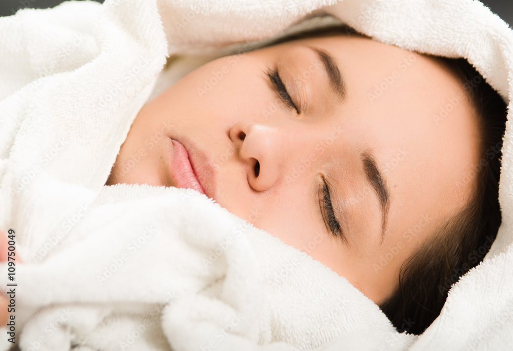 Closeup headshot young woman lying down comfortably, eyes closed with head covered in white towels