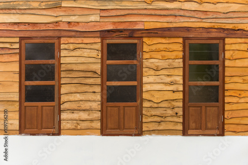 Three wooden doors with black glass stand on the floor leaning against the wooden wall