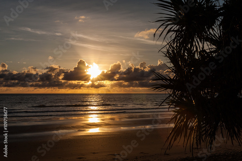 Sunrise peeking over clouds and reflecting over a sandy beach and water