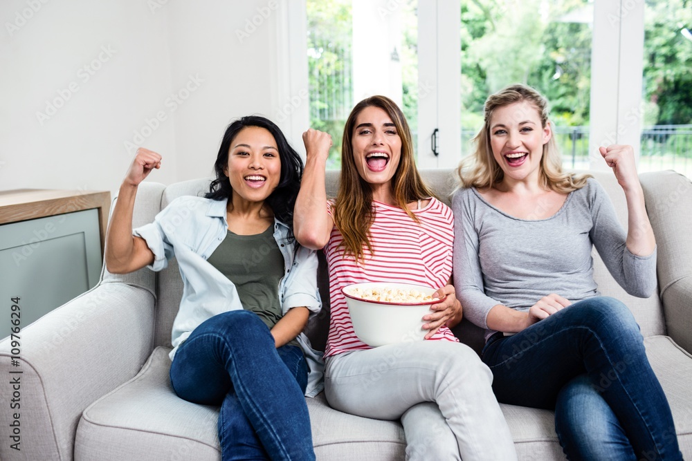 Young female friends cheering while sitting on sofa Young female friends cheering while sitting on sofa