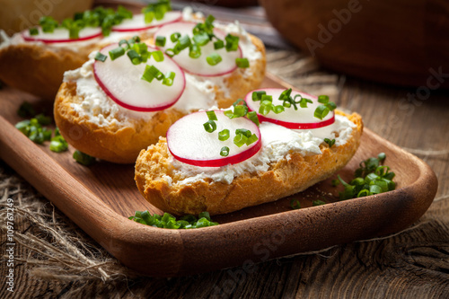 Toasts with radish, chives and cottage cheese on a wooden table.