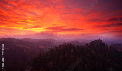 Cold misty morning sunrise in a fall valley of Bohemian Switzerland park. Hill with view hut on hill increased from magical darkness with bloody sky, Mariina vyhlidka, Ceske Svycarsko, Czech Republic