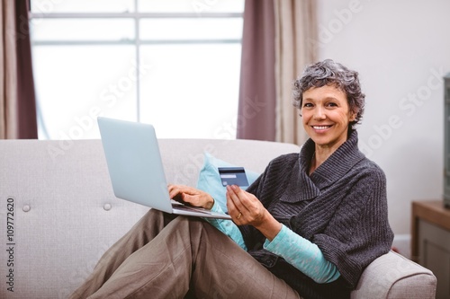 Happy mature woman with credit card using laptop