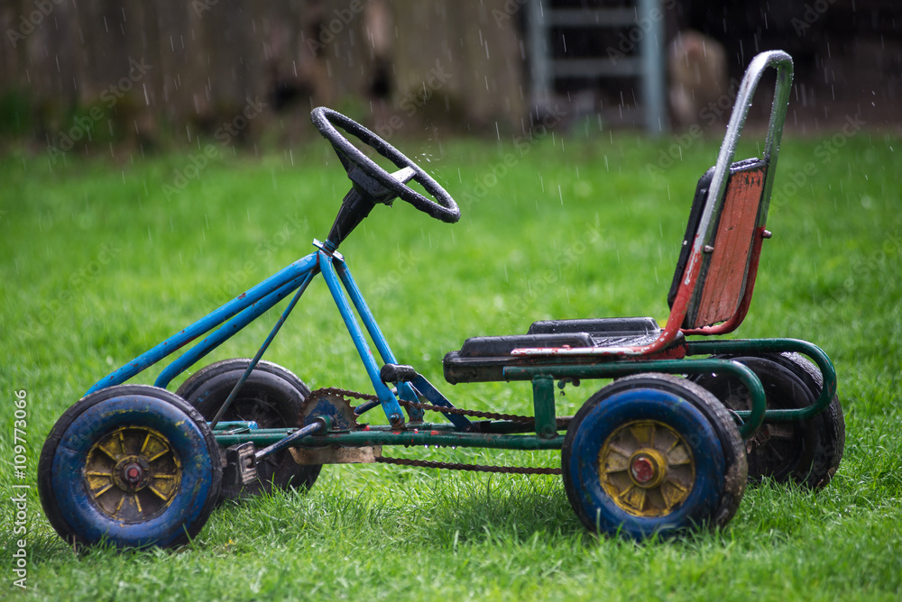 Fototapeta premium Old children's car, standing on green grass in the rain.