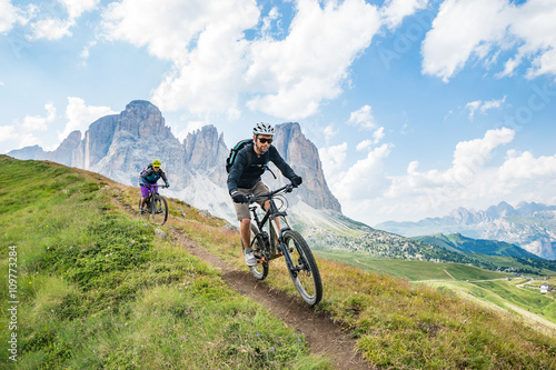 A man and a woman on  mountain bikes racing along trail in the Dolomites,  Val Gardena, Italy photo