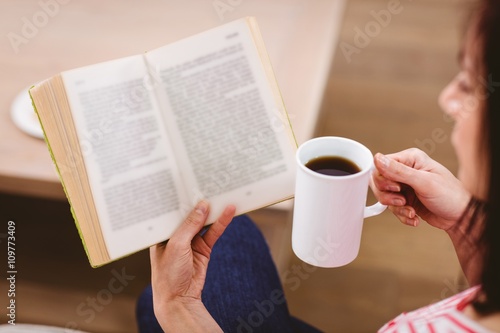 Cropped image of woman reading book while holding coffee cup