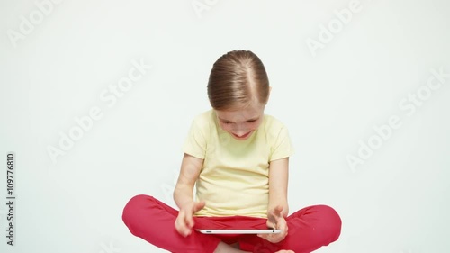 Girl 7-8 years old using tablet pc and laughing and sitting on the white background photo