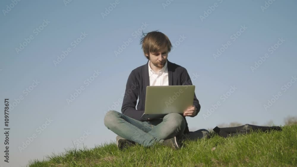Young Man Using Laptop Outdoors Sitting On The Grass In Park Young Man Using Laptop Outdoors Sitting On The Grass In Park
