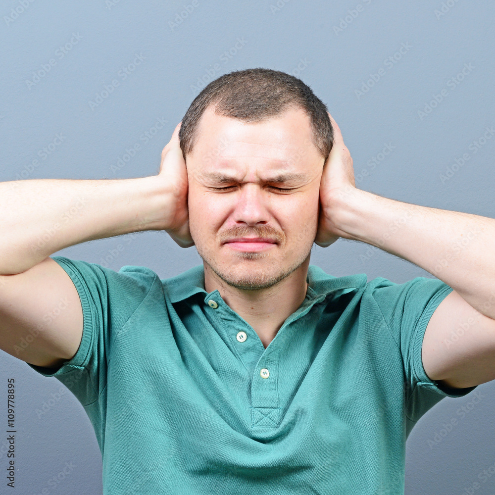 Portrait of man covering ears with hands against gray background