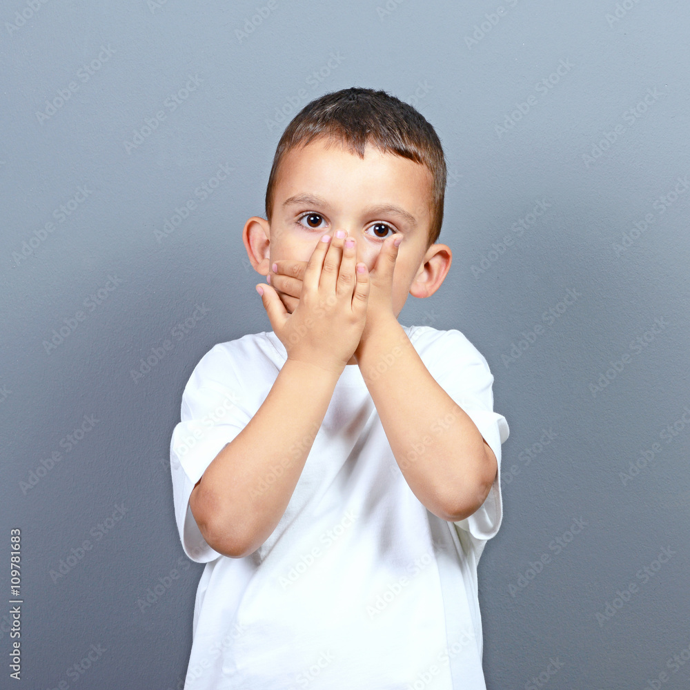 Cute little boy kid covering his face with hands against gray ba Cute little boy kid covering his face with hands against gray ba