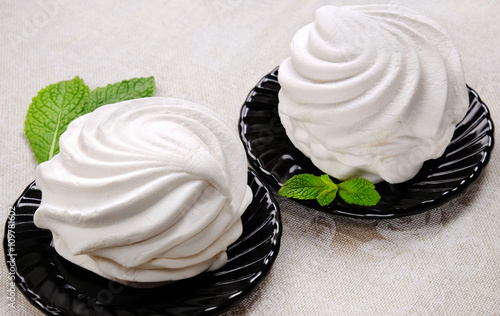 White sweet marshmallow dessert on black saucers with sprigs of fresh mint on linen fabric. photo