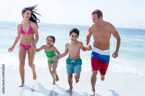 Family running while holding hands at beach 