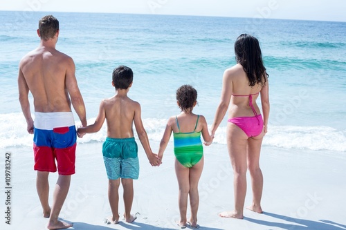 Rear view of family standing on sea shore at beach 