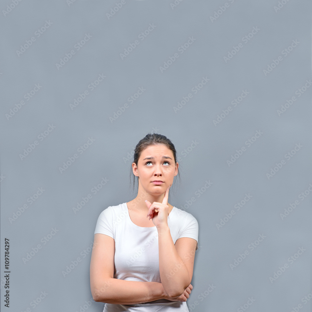 Portrait of thoughtful young woman looking abpve against gray ba Portrait of thoughtful young woman looking abpve against gray ba
