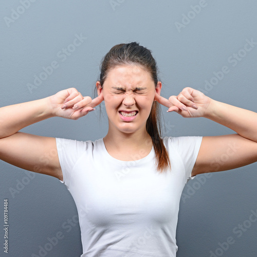 Portrait of woman covering ears with hands against gray backgrou