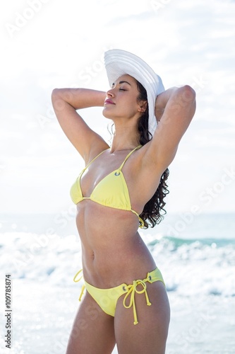 Woman in bikini standing with hands behind head at shore 
