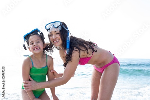 Mother and daughter with diving goggles at beach 