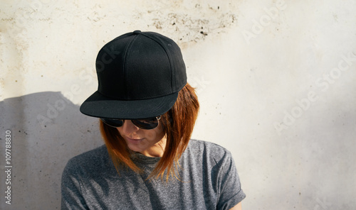 Portrait of a young attractive girl with cap.Female model wearing a black blank cap and sunglasses looking away.