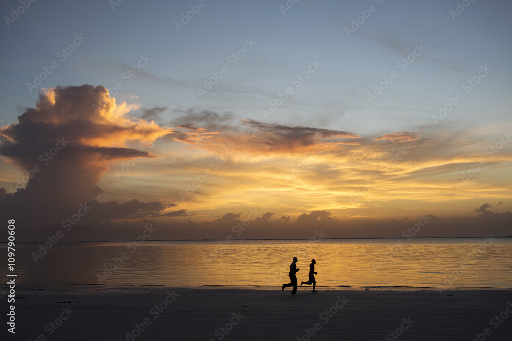 Silhouette of two people jogging on beach at sunrise Silhouette of two people jogging on beach at sunrise