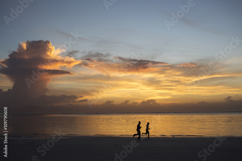 Silhouette of two people jogging on beach at sunrise