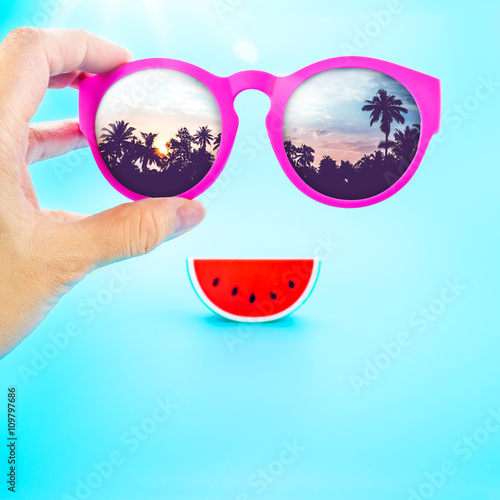 hand holding summer pink glasses with palm tree view and waterme photo