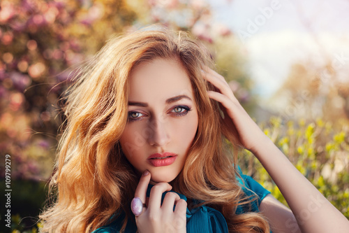 Outdoor close up portrait of a young beautiful lady posing near flowering tree. Model looking at camera. Girl wearing stylish clothes. Female spring fashion & beauty.