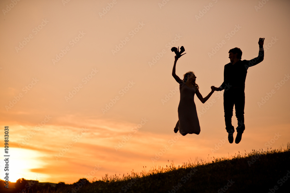 Young couple in love silhouette, a couple jump holding hands at the sunset. Romantic time in the sunset garden